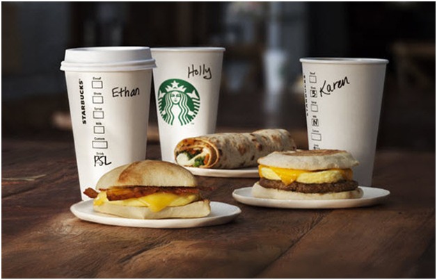 Three Starbucks breakfast sandwiches and coffee cups set on a table